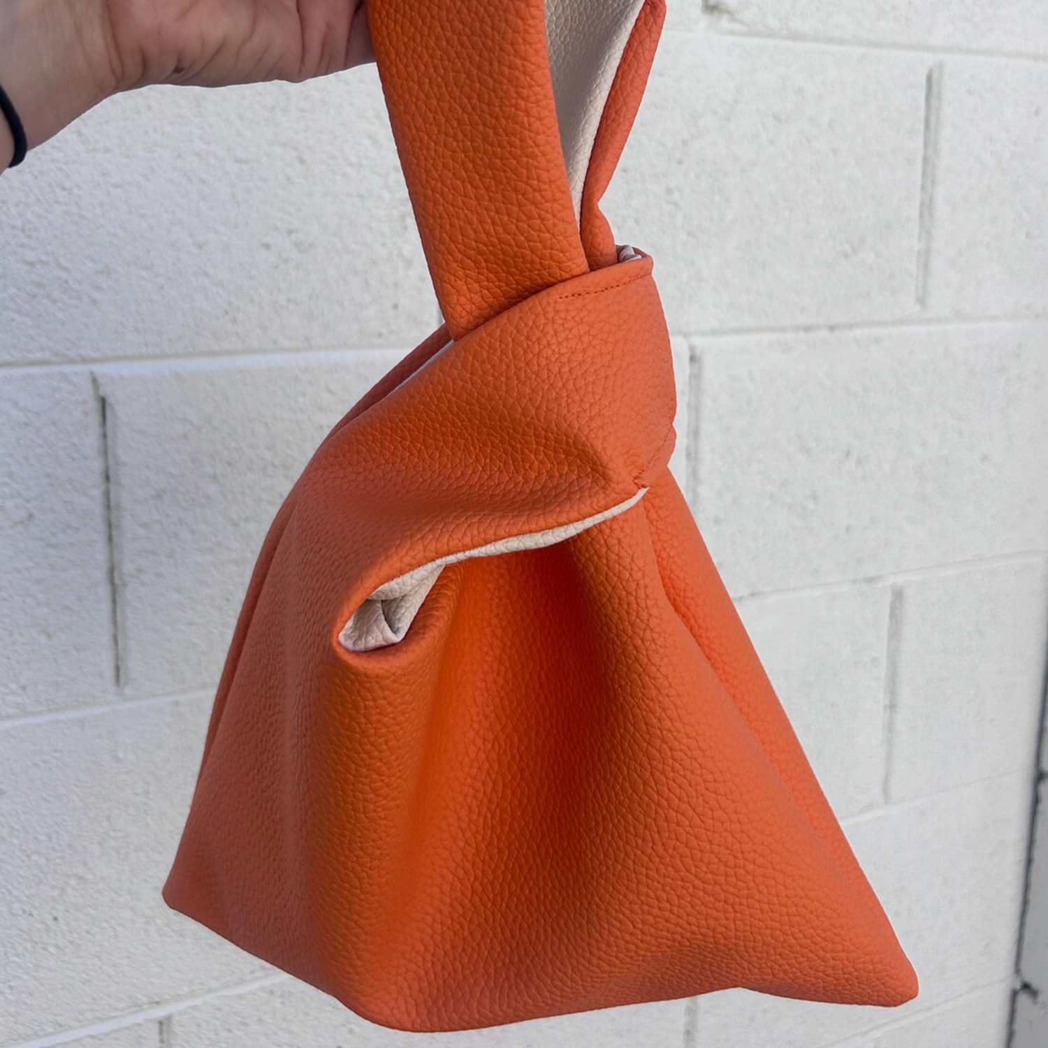 Vibrant Tangerine Orange Pebbled Grain Knotted Wrist Pouch With Contrast Pale Beige Inner Lining And Japanese Wrap Handle Silhouette