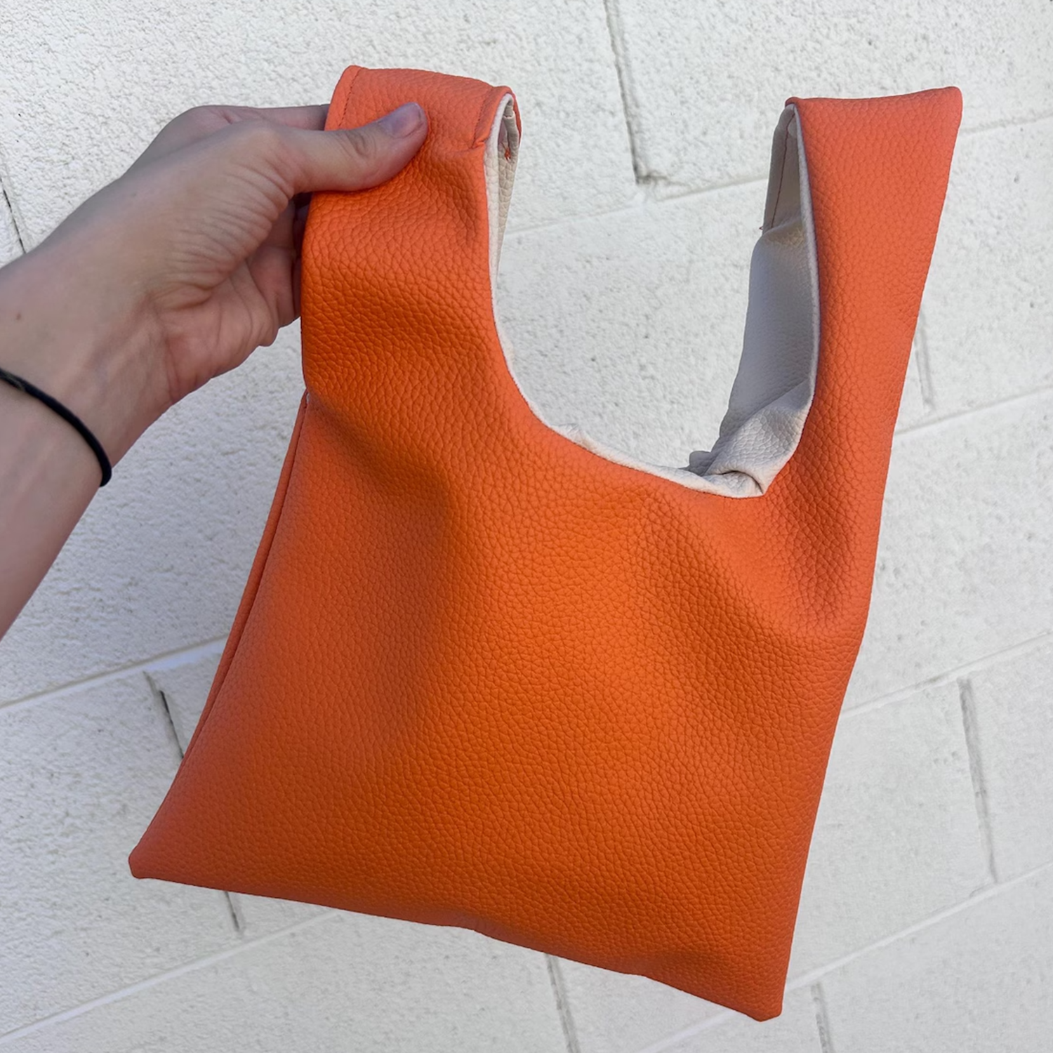 Vibrant Tangerine Orange Pebbled Grain Knotted Wrist Pouch With Contrast Pale Beige Inner Lining And Japanese Wrap Handle Silhouette